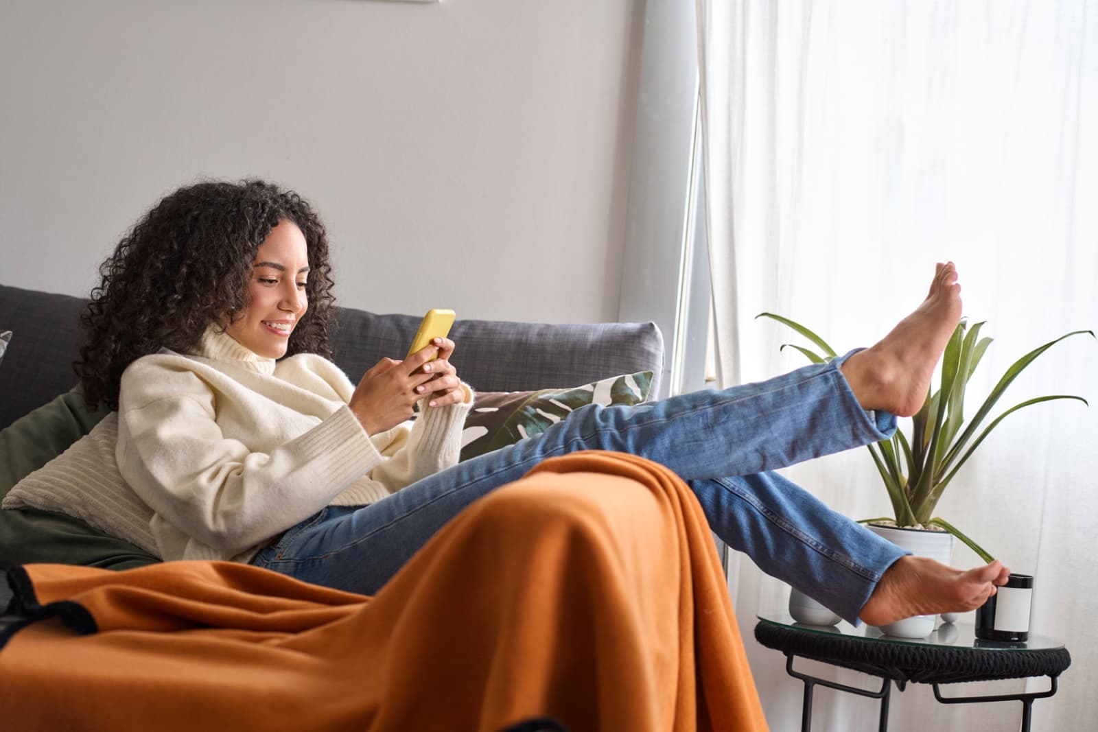 A woman relaxing on a sofa at home, smiling as she looks at her phone